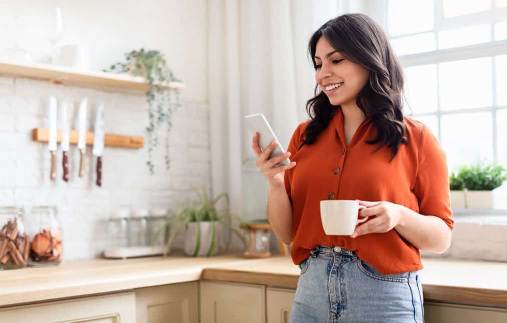Girl looking at phone smiling with a cup of coffee onpoint digital banking