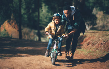 Young father teaching son how to ride bicycle in park