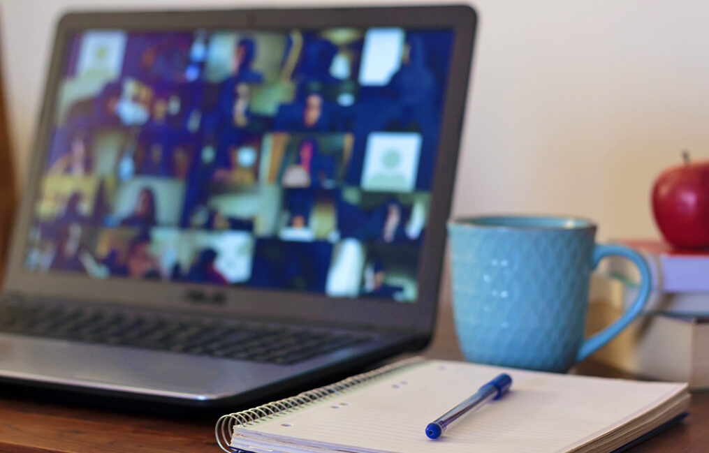 notebook and coffee cup in foreground with laptop and video image blurred in background