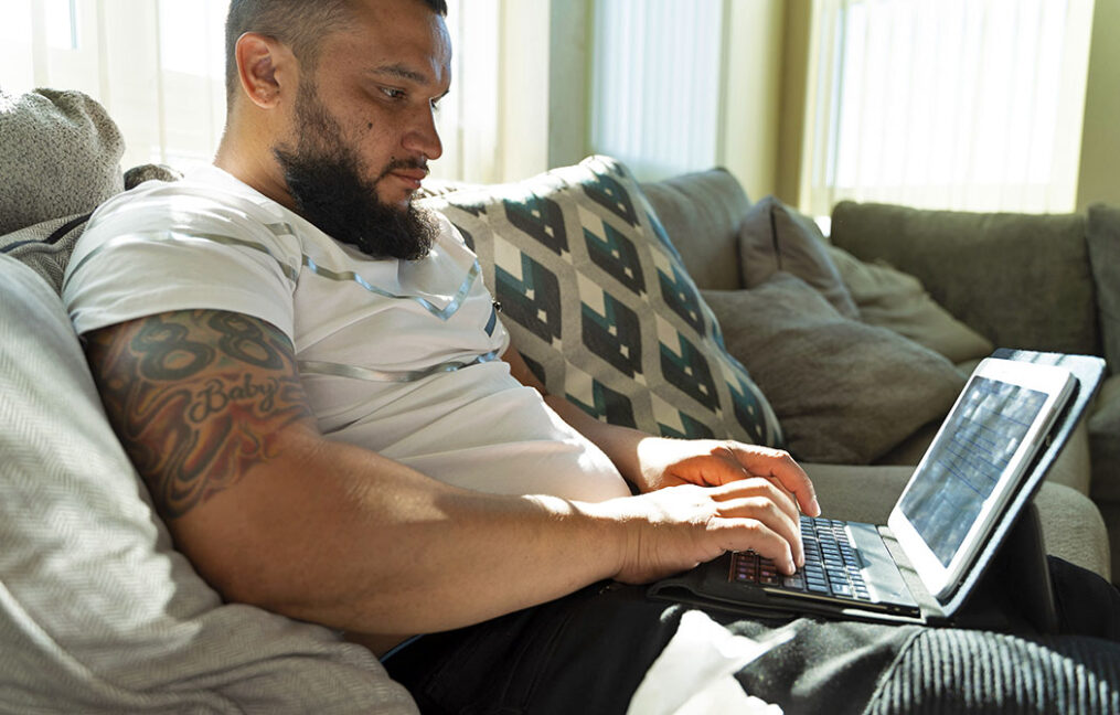 Hispanic man researching on laptop while sitting on couch