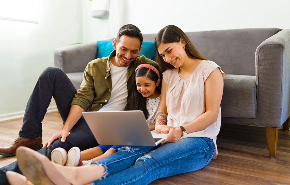 Hispanic family sits in front of couch with laptop sharing financial information with their child