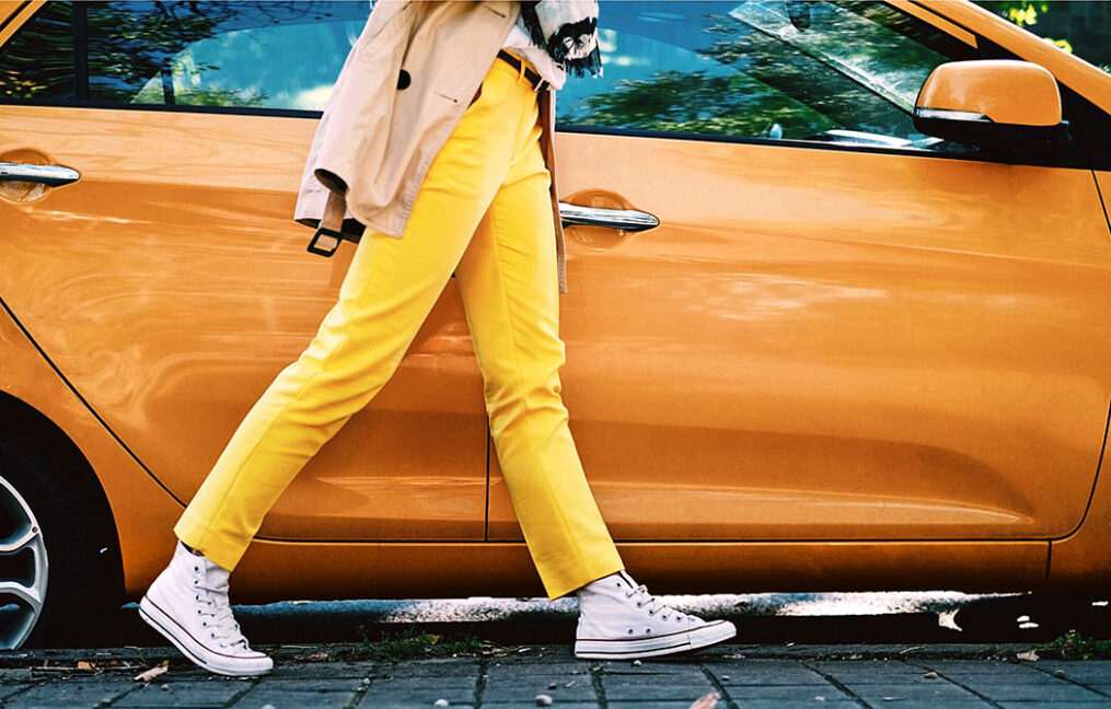 person in bright yellow pants walking past a bright orange car