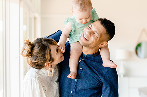 Young family with baby on father's shoulder reaching out for mother's nose.