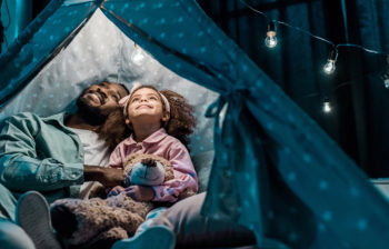 african american father looking up with daughter in wigwam in living room