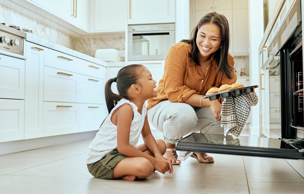 mom pulling muffins out of oven with daughter smiling onpoint heloc june 2025