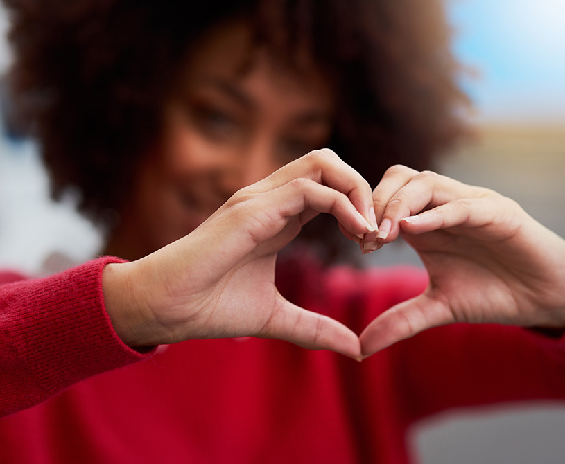 Woman in red sweater holding up hands in shape of a heart.