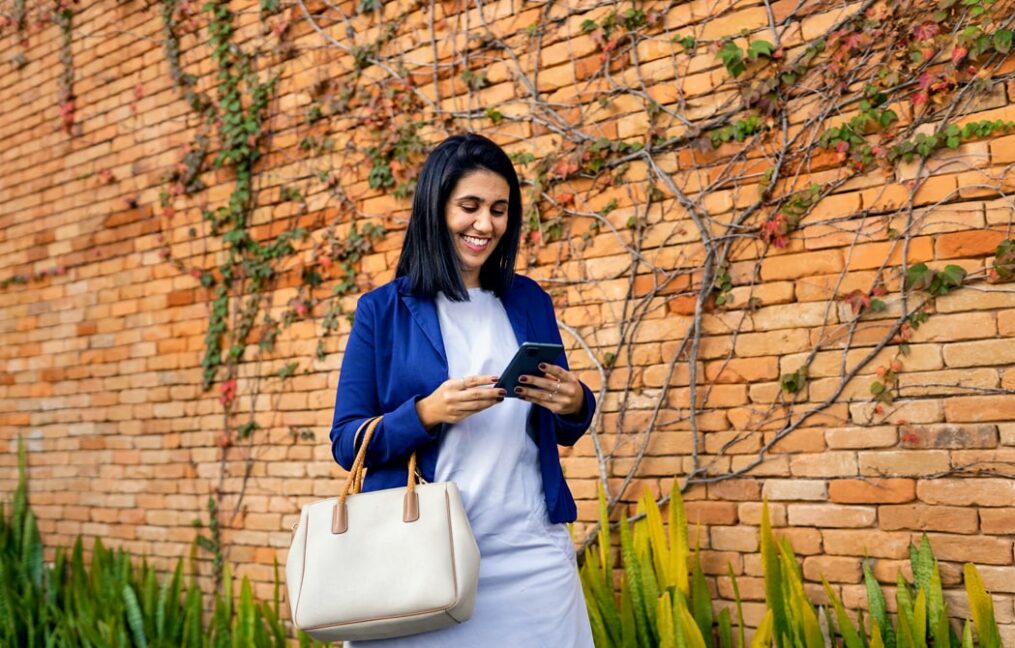 Business Checking-Business woman walking near a brick wall looking at her smartphone