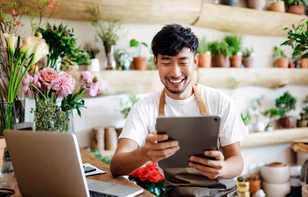 Business digital banking-flower shop employee working from laptop and tablet on business banking needs