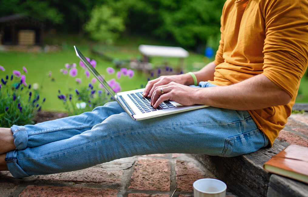 Midsection of unrecognizable man with laptop reviewing a wire transfer outdoors in garden