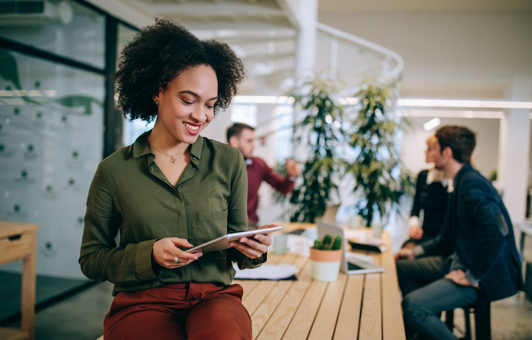 Young professional woman looking at an iPad while her coworkers discuss business in the background