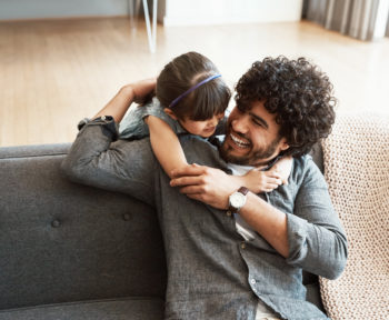 young daughter giving her father a hug on their couch