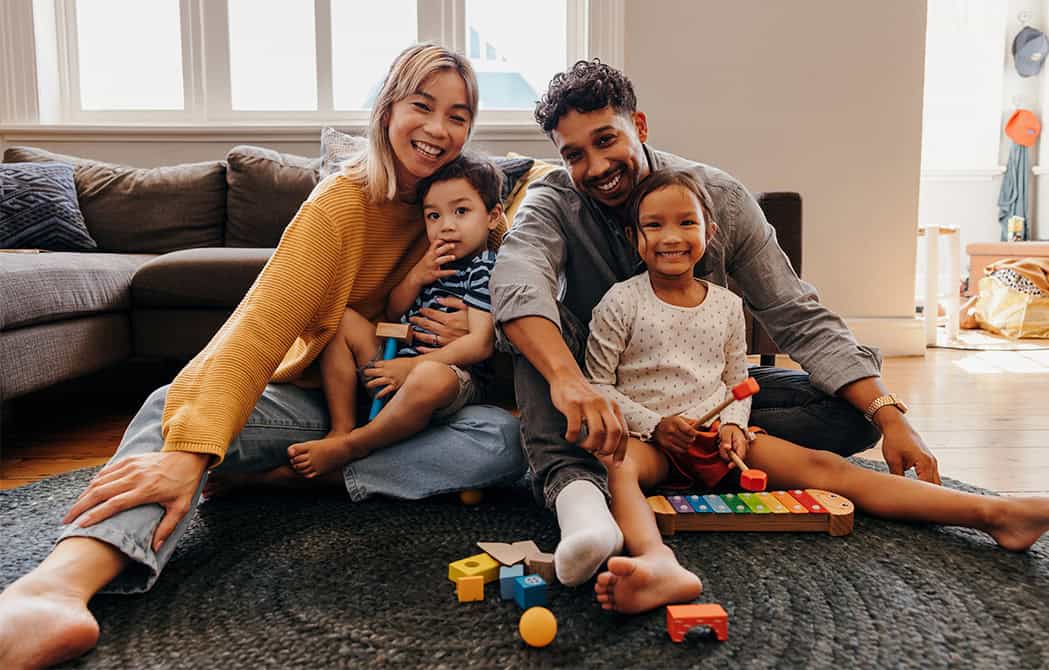 couple with kids sitting on carpet playing with toys smiling homebuyer townhall 2025