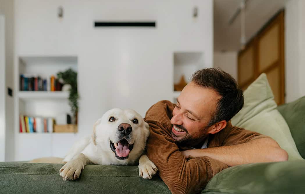man and dog on green couch in home smiling homebuying sept 9