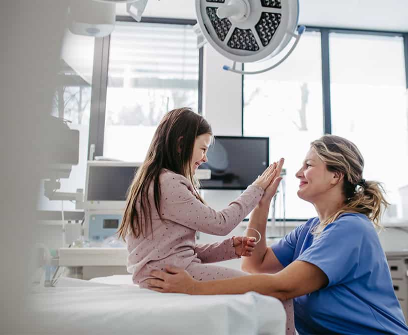 little girl in hospital bed high fiving nurse with smile childrens miracle network