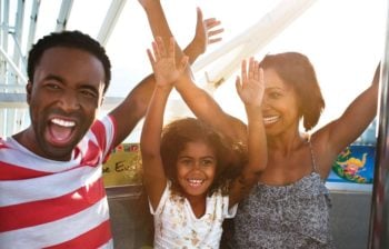 Parents with daughter raising arms and smilling on ferris wheel ride