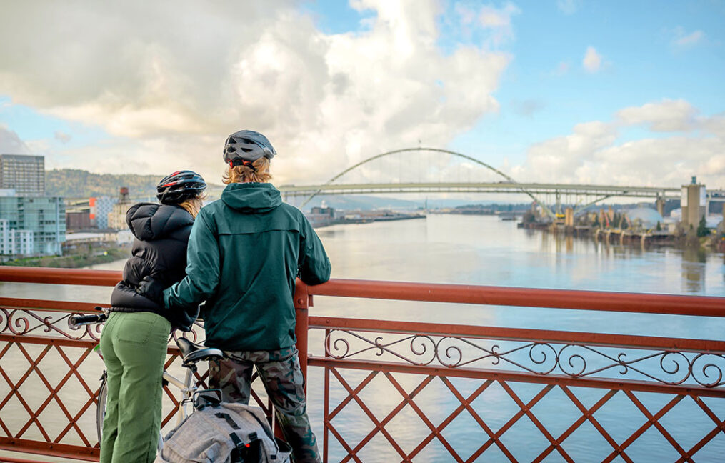 Couple in bike helmets on the Broadway Bridge look over the Willamette River and the Fremont Bridge