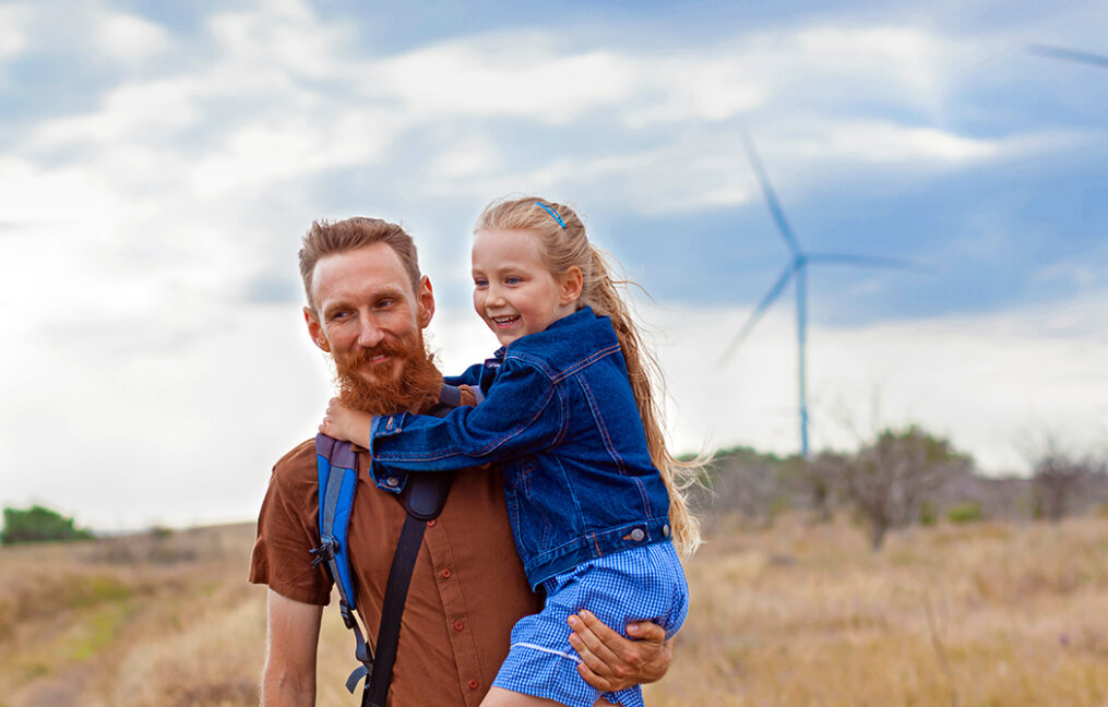 Father with daughter in hands standing on hill with windmill landscape