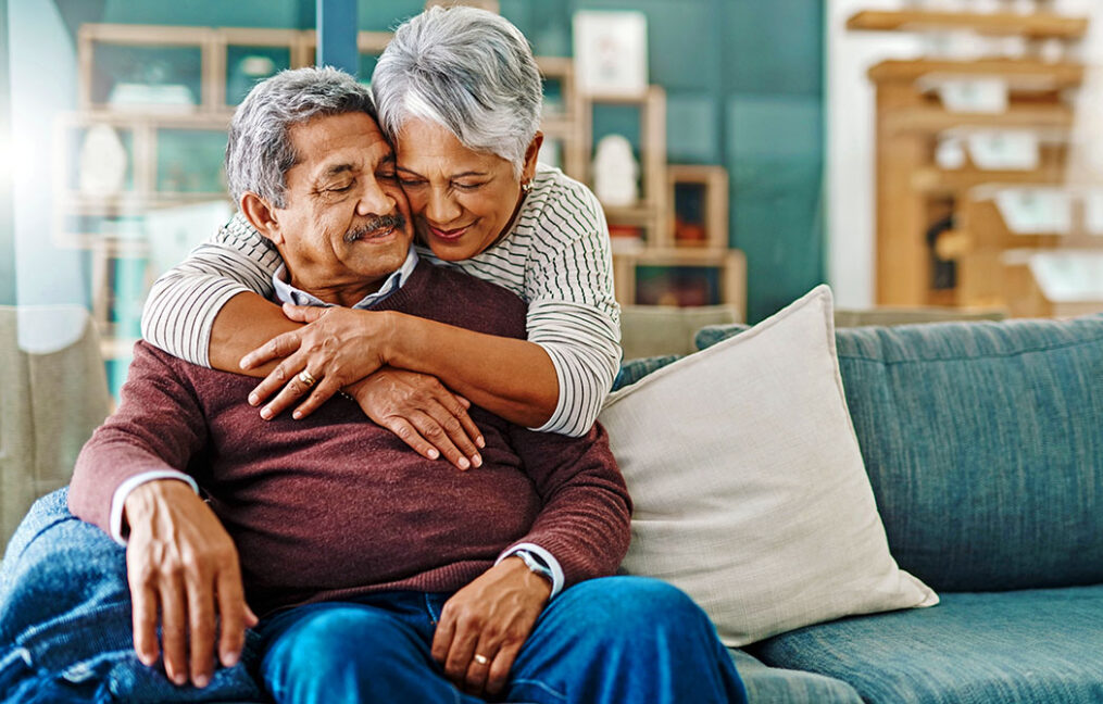 Mature woman hugging her husband sitting on the couch