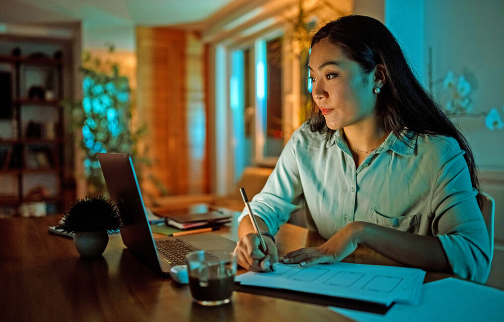 Asian woman taking notes at laptop