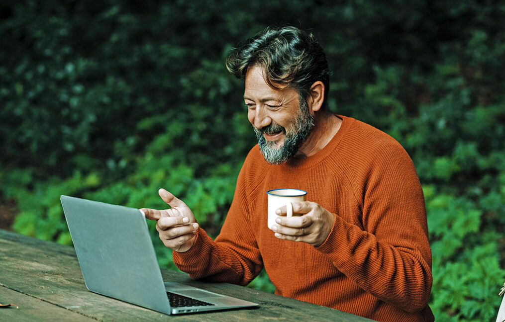 Mature bearded man on laptop video call outdoors