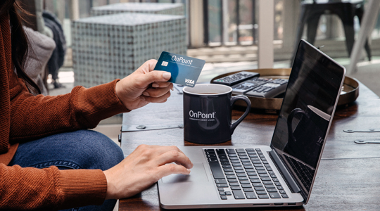 onpoint digital banking-young woman sitting on her couch using her laptop and OnPoint debit card