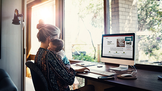 Woman with baby on shoulder looking at onpoint website on desktop computer