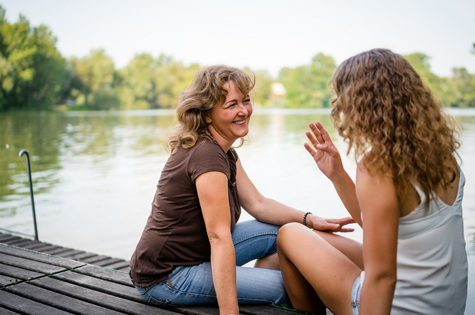 Mom and daughter sitting and talking on a dock at the lake