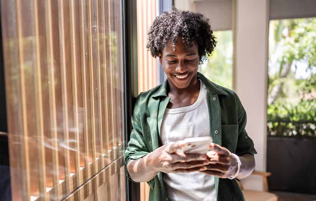 man smiling looking at phone in green shirt with natural light