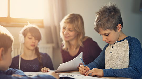 Little boy aged 7 and his teenage sister are doing homeworks. The girl is wearing headphones and the boy is writing in his excercis book with a fountain pen.