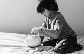 Young boy putting money in a white piggy bank