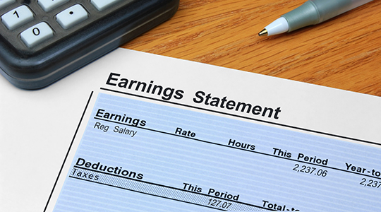 An itemized earnings statement showing earnings and deductions, on a desk with a calculator and pen.