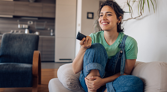 Young woman sitting on the sofa, watching TV at home and enjoying.