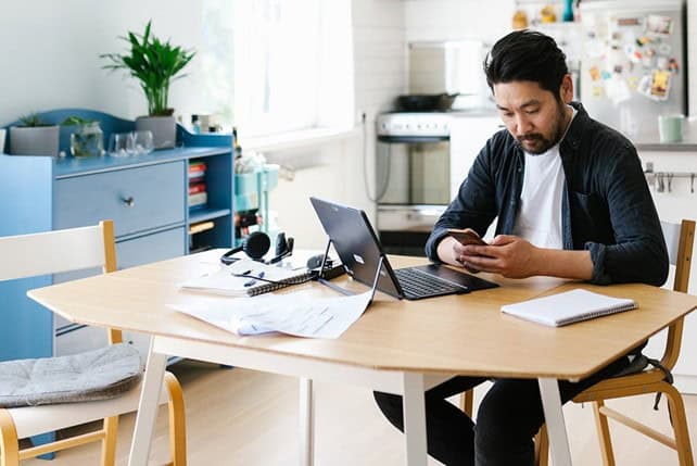 man looking at phone at desk doing paper work