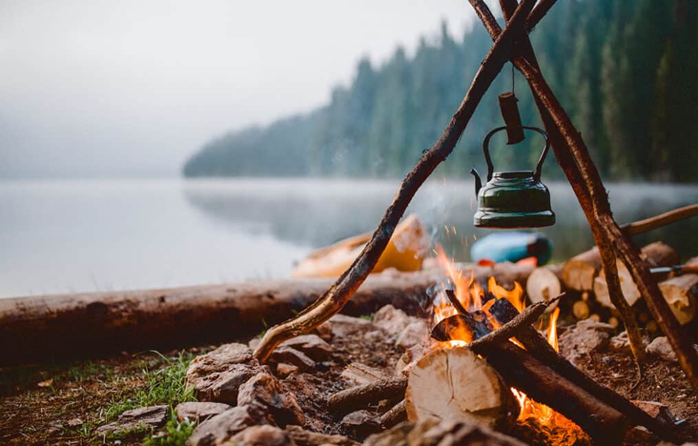 Kettle warming up on fire next to lake