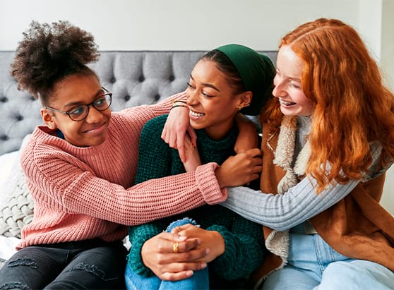 three-girls-sitting-on-a-bed-hugging-each other