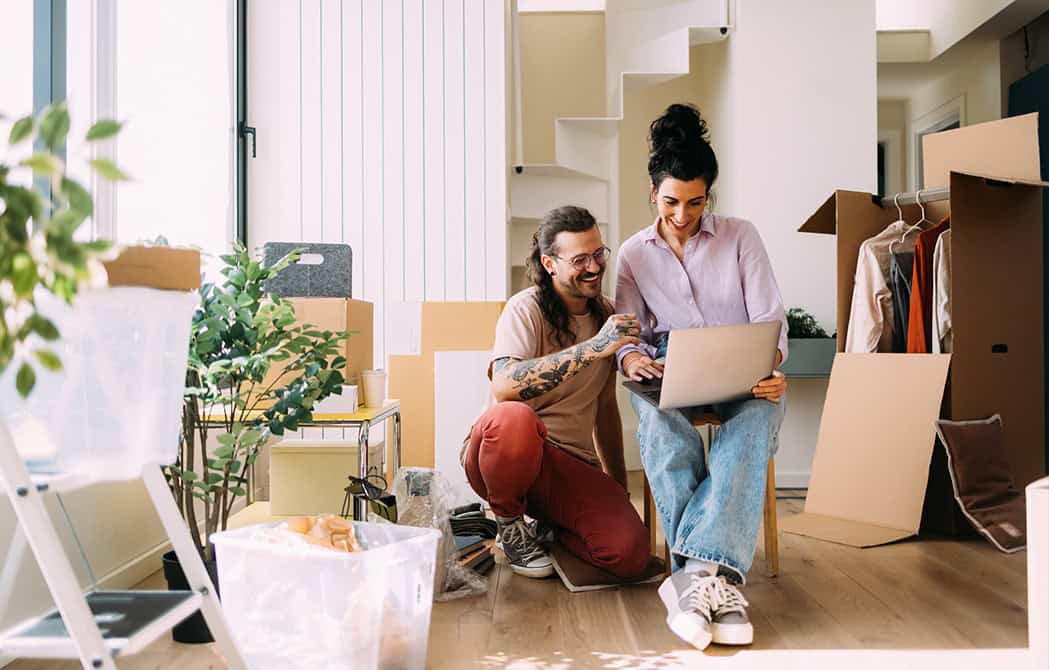 younger couple moving into new home happy looking at laptop