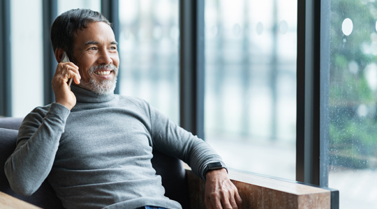Smiling happy mature asian man with white stylish short beard using smartphone