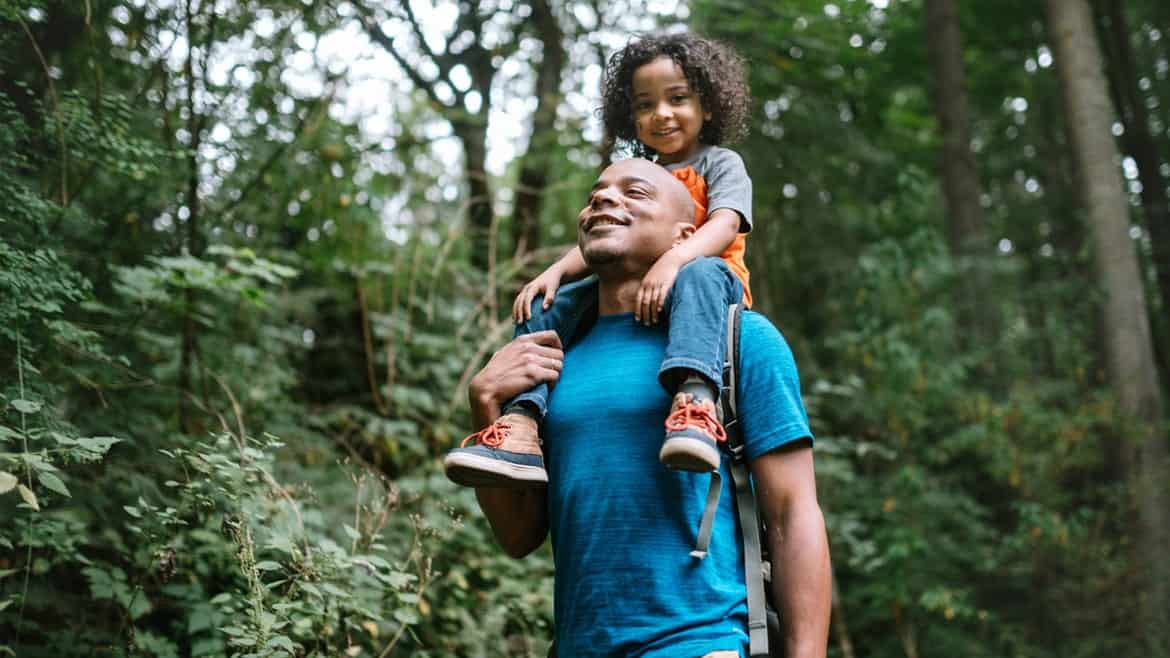 _father-carries-son-on-hike-through-forest-trail-in-pacific-northwest