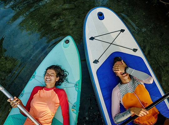 onpoint summer skip pay two woman laughing laying on paddle boards