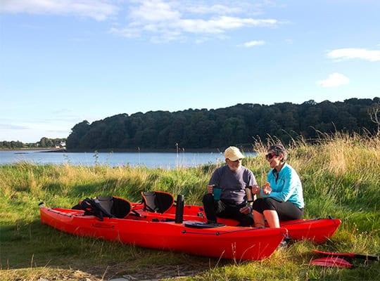 older couple with cup of coffee sitting on lake with kayak onpoint summer skip pay 2025