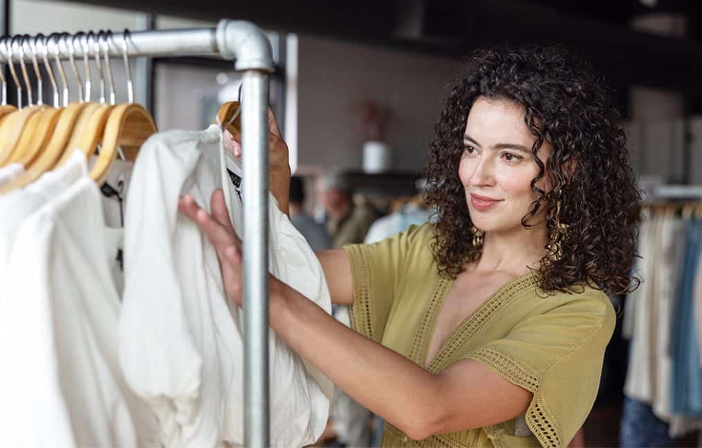 insert alt text: example small business owner looking through white shirts on rack onpoint credit union support local