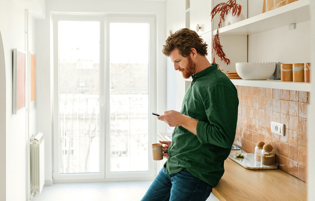 security page-hero-bearded man leaning against counter in kitchen looking curiously at his phone