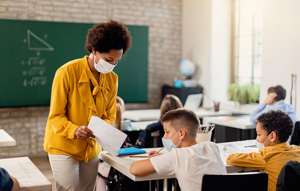 masked teacher shares paper with masked student