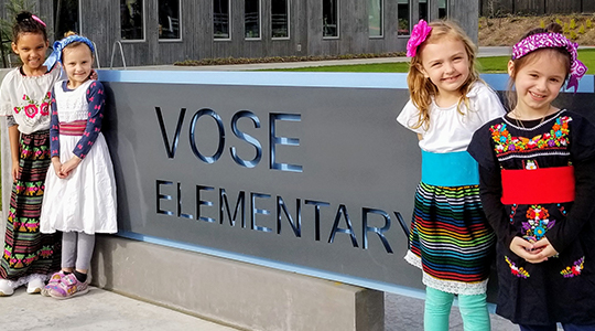 four kids in front of school sign