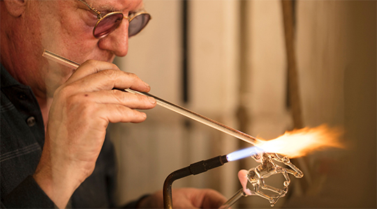 man working with glass to create a glass horse.