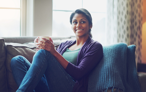 Young woman sitting on her couch enjoying a cup of coffee