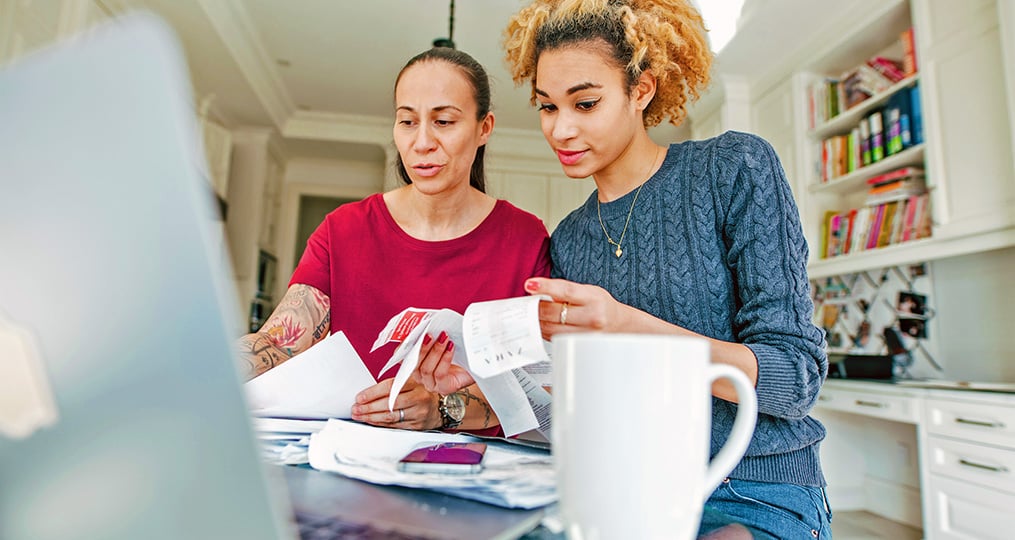 two women review receipts and tax documents at laptop on kitchen counter