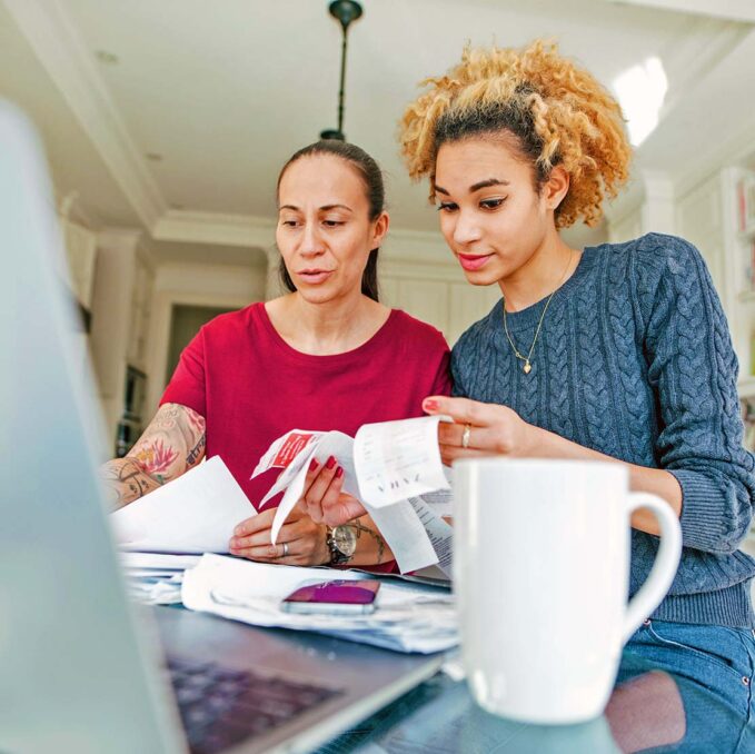 two women review receipts and tax documents at laptop on kitchen counter