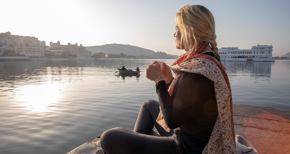 mature woman sits outside looking at the sunset with coffee in her hand