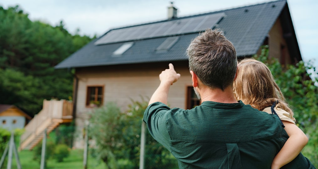 rear view of dad holding a little girl in his arms and showing her a house